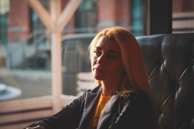 Cafe pencere gün ışığı tarafından. Bir kafede bir masada oturan sarışın bir kız romantik görüntü pencereden dışarı katlanmış elleriyle görünüyor..