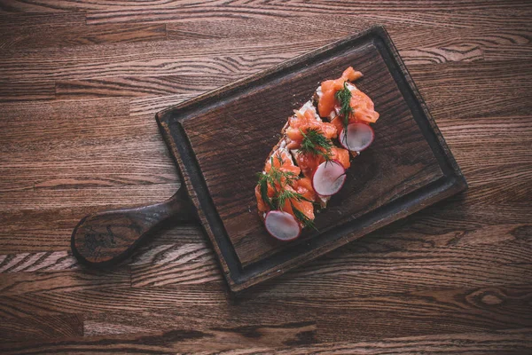 Cafe By the window daylight. A wooden tabletop on which lies a board of sandwiches with salmon greens.