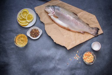 Çiğ balık ile baharat. Bir koyu gri masa üzerinde bir kulübe balık kraft kağıt üzerinde bir tabak limon karabiber tuz ve baharat ve yağ ile yatıyor..