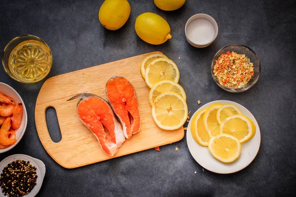 Raw fish with seasonings. Wooden board in the middle of the frame with the salmon laid out in a plate raw shrimp pepper lemon slices with seasoning oil.