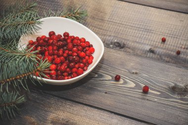 Festival bileşimi yılbaşı Kartpostal arka plan için. Ahşap masa üstü bir tabak taze pişmiş kek ile kırmızı meyveler ile dekore edilmiş bir ışık beyaz toz ve çam çırpı ile kırmızı meyveler bir tabak serpilir.