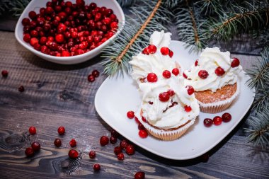 Festival bileşimi yılbaşı Kartpostal arka plan için. Taze pişmiş pasta beyaz bir plaka üzerinde kırmızı meyveler ile dekore edilmiş ve kırmızı meyveler hafif ahşap masa üst Ladin dal ile süslenmiş ile tepesinde bir plaka ile beyaz krem şanti.