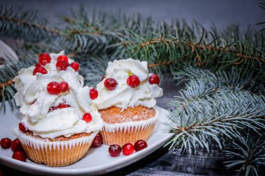 Festival bileşimi yılbaşı Kartpostal arka plan için. Taze pişmiş pasta beyaz bir plaka üzerinde kırmızı meyveler ile dekore edilmiş ve kırmızı meyveler hafif ahşap masa üst Ladin dal ile süslenmiş ile tepesinde bir plaka ile beyaz krem şanti.