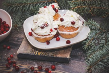 Festival bileşimi yılbaşı Kartpostal arka plan için. Taze pişmiş pasta beyaz bir plaka üzerinde kırmızı meyveler ile dekore edilmiş ve kırmızı meyveler hafif ahşap masa üst Ladin dal ile süslenmiş ile tepesinde bir plaka ile beyaz krem şanti.