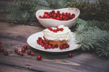 Festival bileşimi yılbaşı Kartpostal arka plan için. Taze pişmiş pasta beyaz bir plaka üzerinde kırmızı meyveler ile dekore edilmiş ve kırmızı meyveler hafif ahşap masa üst Ladin dal ile süslenmiş ile tepesinde bir plaka ile beyaz krem şanti.