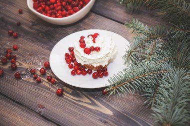 Festival bileşimi yılbaşı Kartpostal arka plan için. Taze pişmiş pasta beyaz bir plaka üzerinde kırmızı meyveler ile dekore edilmiş ve kırmızı meyveler hafif ahşap masa üst Ladin dal ile süslenmiş ile tepesinde bir plaka ile beyaz krem şanti.