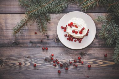 Festival bileşimi yılbaşı Kartpostal arka plan için. Taze pişmiş pasta beyaz bir plaka üzerinde kırmızı meyveler ile dekore edilmiş ve kırmızı meyveler hafif ahşap masa üst Ladin dal ile süslenmiş ile tepesinde bir plaka ile beyaz krem şanti.