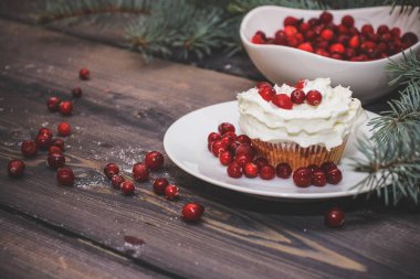 Festival bileşimi yılbaşı Kartpostal arka plan için. Taze pişmiş pasta beyaz bir plaka üzerinde kırmızı meyveler ile dekore edilmiş ve kırmızı meyveler hafif ahşap masa üst Ladin dal ile süslenmiş ile tepesinde bir plaka ile beyaz krem şanti.