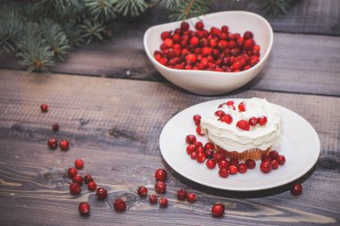 Festival bileşimi yılbaşı Kartpostal arka plan için. Taze pişmiş pasta beyaz bir plaka üzerinde kırmızı meyveler ile dekore edilmiş ve kırmızı meyveler hafif ahşap masa üst Ladin dal ile süslenmiş ile tepesinde bir plaka ile beyaz krem şanti.