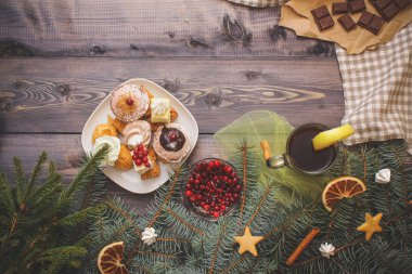 Mutlu yeni yıl çam dalları gingerbread yıldız ile dekore edilmiş, tarçın sopa, kurutulmuş portakal dilimleri ve beze tepeler, parlak kızılcık, tatlılar tatlı tabağı, kraft kağıt üzerinde kırık çikolata ve bir bardak çay limon keten napki üzerinde