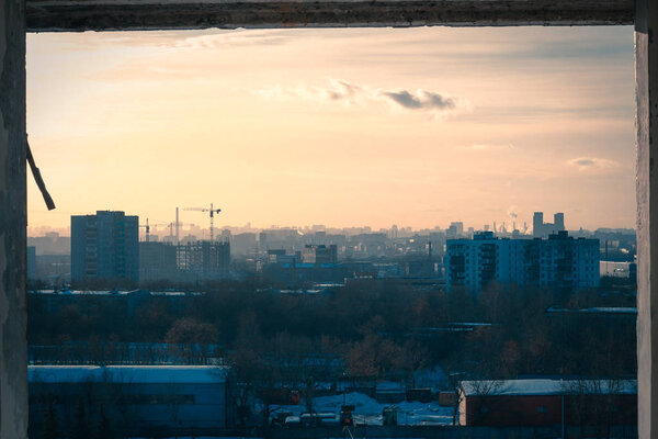 View of the city panorama in the rays of the setting sun from the window of an abandoned factor