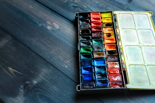 On a dark gray wooden tabletop, juicy watercolor paints, which t — Stock Photo, Image