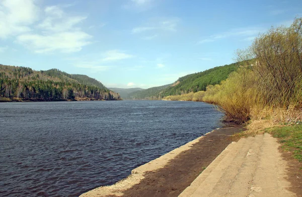 Wide concrete steps lead to the river. There is an amazing view of the water ripples and wooded hills in the distance.