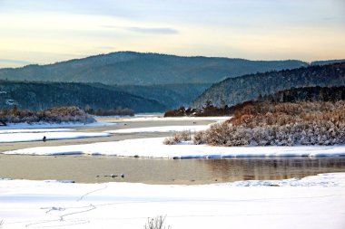 Kış manzarası - nehir karlı kıyılar ve odunsu tepeler arasında akar.