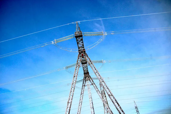 Mavi gökyüzü arka planında gerilmiş kabloları olan elektrik hattı direğinin çelik yapısı.