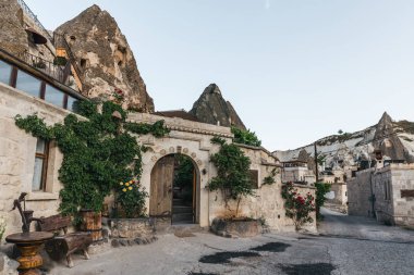 traditional buildings with green plants and beautiful rock formations in cappadocia, turkey  clipart