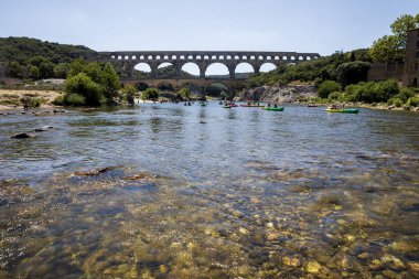 PROVENCE, FRANCE - JUNE 18, 2018: Pont du Gard (bridge across Gard) and people swimming on boats in Provence, France clipart