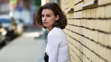 Şehirde dinlenen güzel bir kız, binanın duvarına yaslanmış. El kamerası.