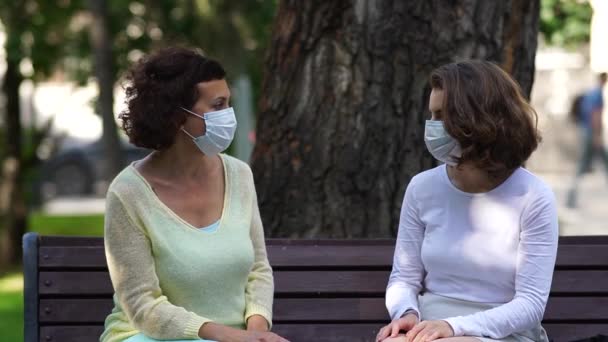 Máma a dcera v lékařských maskách mluví na lavičce. — Stock video