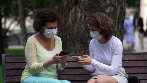 Mamma och dotter i medicinska masker pratar på en bänk. — Stockvideo