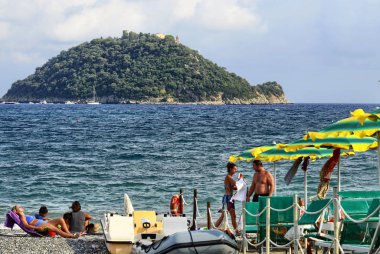 Albenga, Liguria, Italy. July 2018. The Gallinara island is a landmark on the beaches around Albenga. Its unmistakable shape is reminiscent of a large turtle. Swimmers can enjoy the view. clipart