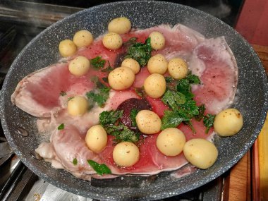 Taze maydanoz yaprakları ile terbiyeli kılıç balığı, dilim pişirme Pan yeni patates, biber. Pişirme dilimleri taşır, biraz pan dan yükselir.