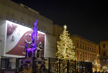 Bologna, Emilia Romagna, Italy. December 2018. The Neptune fountain at night, for the New Year's Eve, is illuminated with changing lights and has been fenced off. Behind a large illuminated Christmas tree.