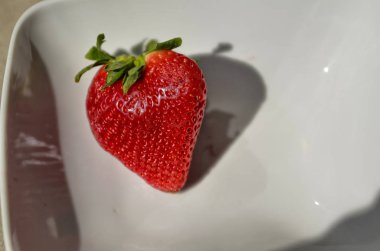 Parlak kırmızı çilek ile beyaz bir tabak.