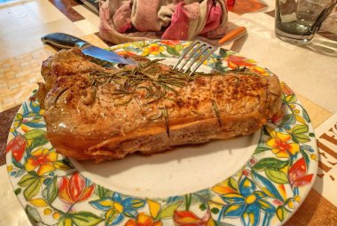 Büyük bir sığır eti biftek pişmiş ve biberiye ile terbiyeli. Hala tabakta sigara, bıçak ve çatal dilim için hazırız. Arka planda tablo ayarlanır.