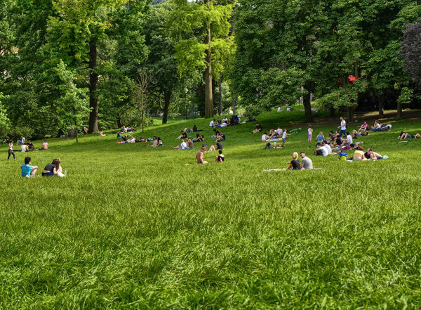 Turin, Piedmont, Italy.June 2018. At the Valentino park people enjoy the wonderful day. Couples and groups of friends relax on the large green lawn surrounded by trees.