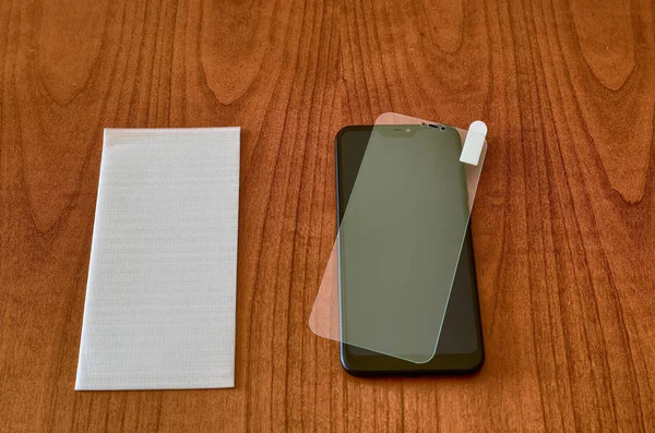 On the wooden table, the smartphone and the protective glass cov