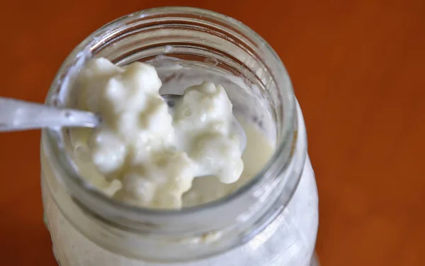 A teaspoon stirs the kefir and raises some granules in a close-u — Stock Photo, Image