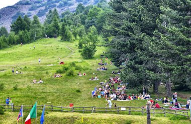 Colle del Lys, Piedmont, İtalya. Temmuz 2019. Serinletimi arayan insanlar piknik için büyük yeşil bir çim ile dağın yamacından yararlanırlar. Bulutların geçişi tanınabilir.