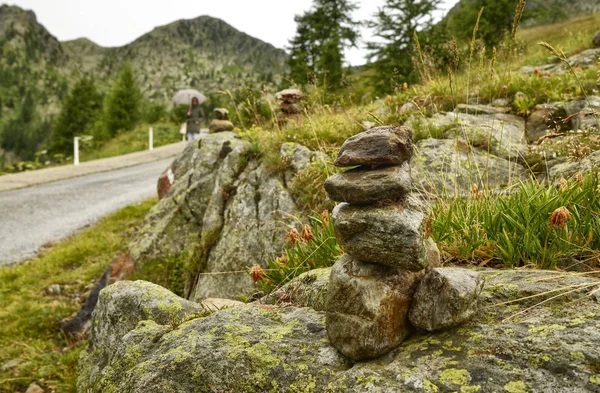 Stones piled up as a Zen memorial along a mountain road, in the background a blurred road and an indistinguishable woman.