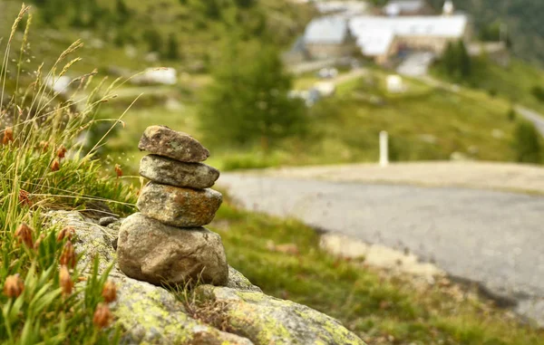 Taşlar bir dağ yolu boyunca zen anıt olarak yığılmış, arka planda bir ilçe bulanık ve ayırt edilemez.