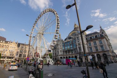Antwerp, Flanders, Belçika. Ağustos 2019. Tren istasyonunun yanında bir dönme dolabın kurulduğu büyük bir meydan var. Beyaz bulutlu mavi gökyüzü. İnsanlar.