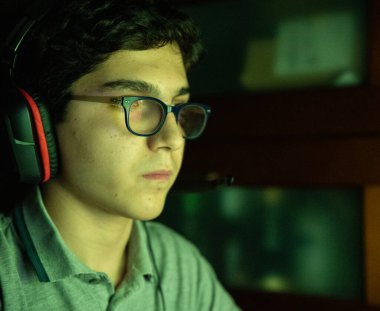 Video oyun oturumu sırasında oyun hareketi. Dalgalı siyah saçlı ve gözlüklü beyaz çocuk oyun sırasında ekranın renklerini değiştirerek yüzünü aydınlattı. Oyun kulaklığı tak..