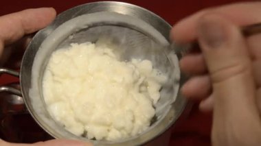 Kefir döküyorum. Mayalanmış süt ve granüllerin karışımı kevgire dökülerek işlenir.