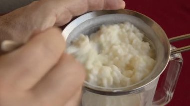 Kefir granüllerini yakından çek, çocuğun elleri nazikçe onları tutuyor. Eller taneciklerin kasenin içine kaymasına izin verdi.. 