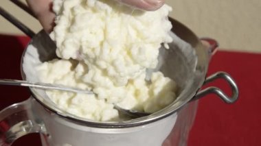 Kefir kaşıkla süzgeçten geçiyor. Sürahinin altına beyaz ve kremalı kefir damlıyor.