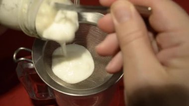 Kefir döküyorum. Mayalanmış süt ve granüllerin karışımı kevgire dökülerek işlenir.