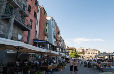 Portovenere, Liguria, İtalya. Haziran 2020. Renkli cepheli güzel evlerin önündeki gezinti güvertesi: deniz kenarında yürüyen insanlar..