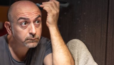 Orta yaşlı beyaz bir adam banyoda saçını kesiyor. Kırpıcıyı kafana yerleştirirken aynada gözlerinle kontrol et..