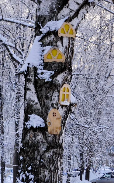 A large trunk of snow-covered wood on which are made of plywood round, carved Windows and doors for children to play.