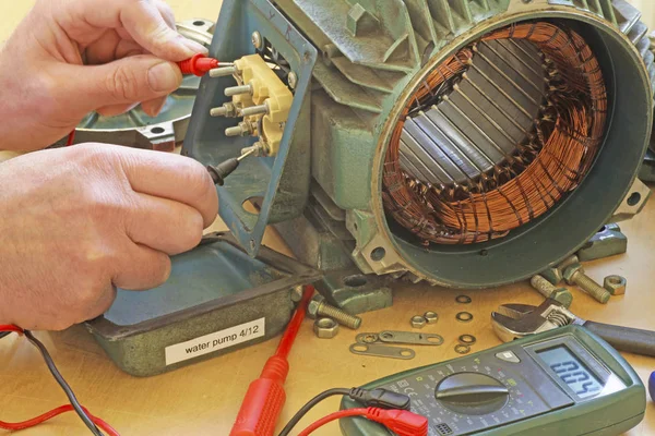 Three phase induction   motor bearing repair  A fitter/technician  checking motor windings resistance readings with a multimeter.