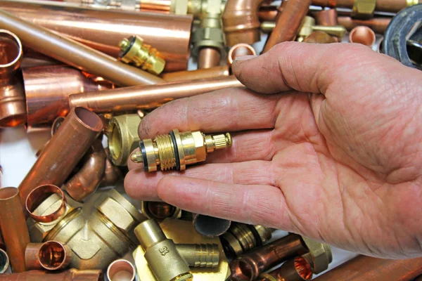 plumbers fittings and pipes  a mans hand holding a tap head gear over pipes and fittings