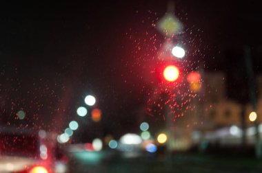 Kırmızı ışık. Arabanın ön camdan görüntüleyin. Camına yağmur damlaları. Bulanık fotoğraf. Gece şehir.