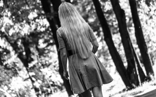 Monochrome photography. Girl in the Park for a walk. Long hair, summer dress. Beautiful background. Sunny day. Girl on walk. Stay in the Park. Tracking. The view from the back. Girlish figure.