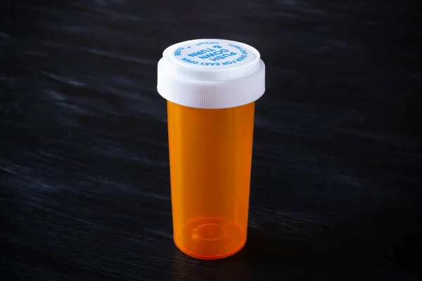 Empty orange prescription bottle with white cap on a dark surface.