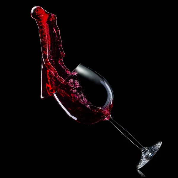 黒い背景に隔離されたスプラッシュと赤ワインのためのガラス. — ストック写真